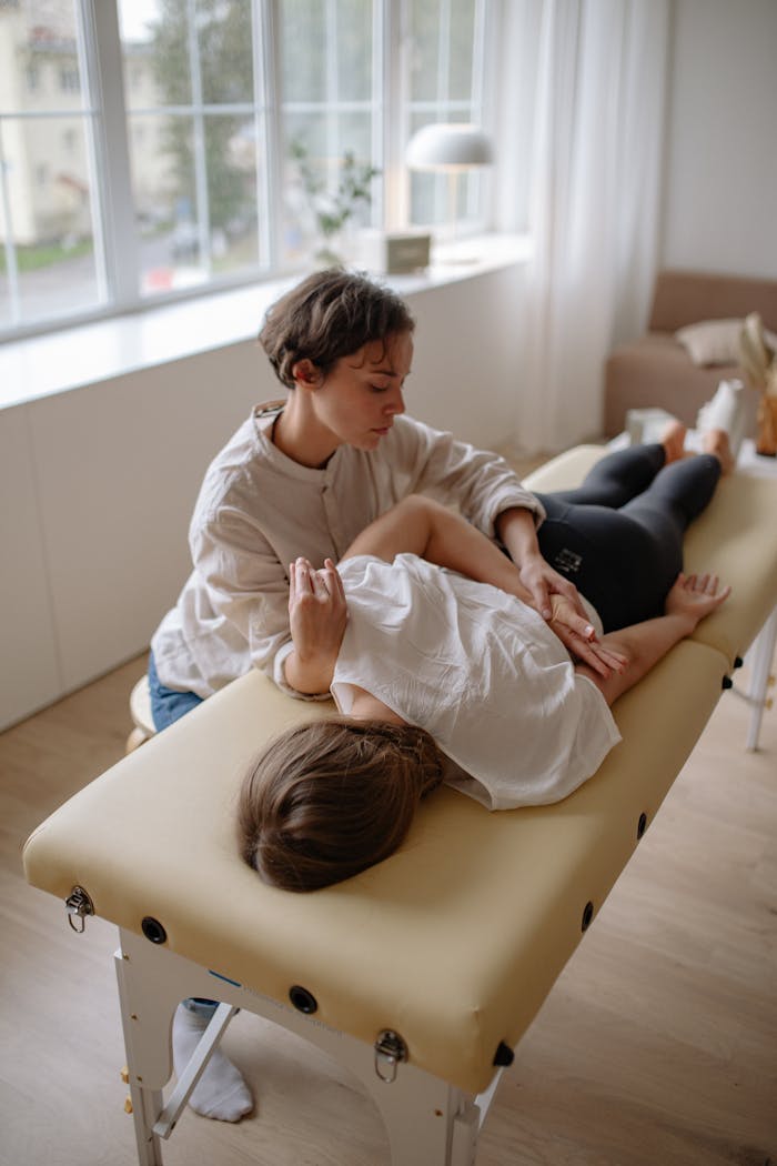 our-services-1 A woman lying on a massage table receiving a chiropractic adjustment in a bright room.