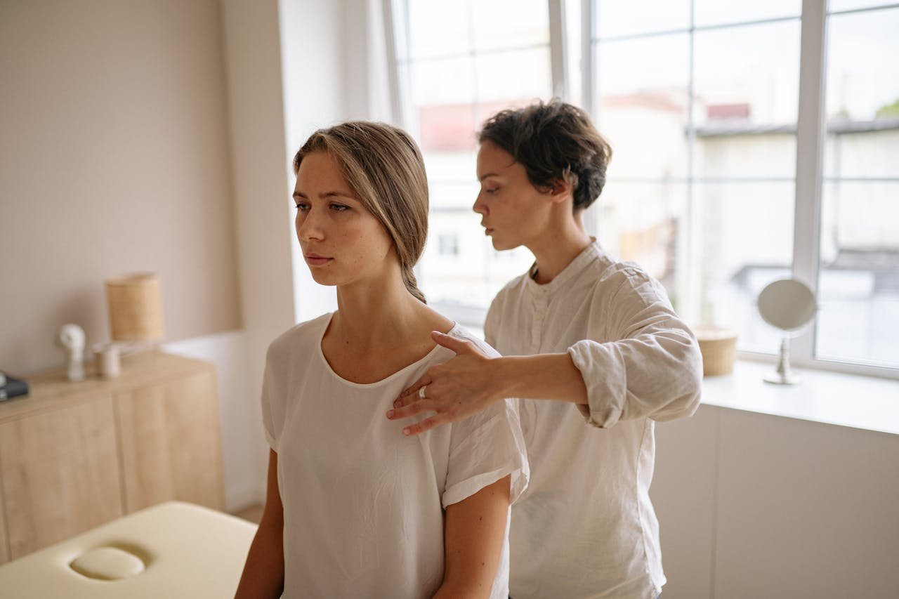 our-services-2 A woman receives shoulder therapy from a therapist in a serene room with natural light.